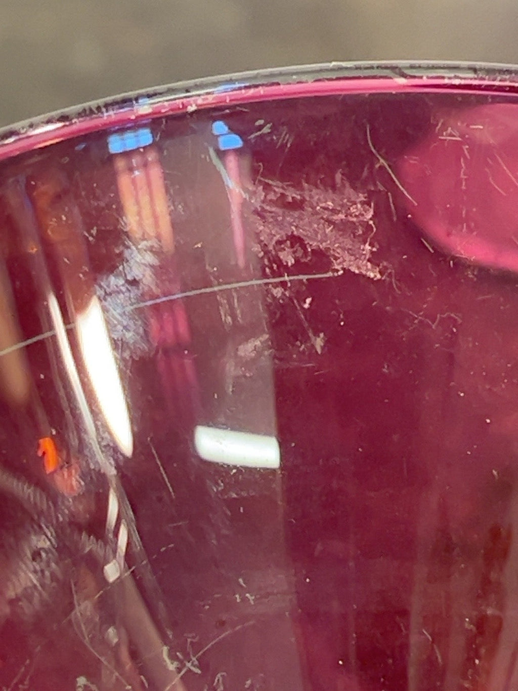 Close-up of surface scratches and wear on ruby red cocktail glass