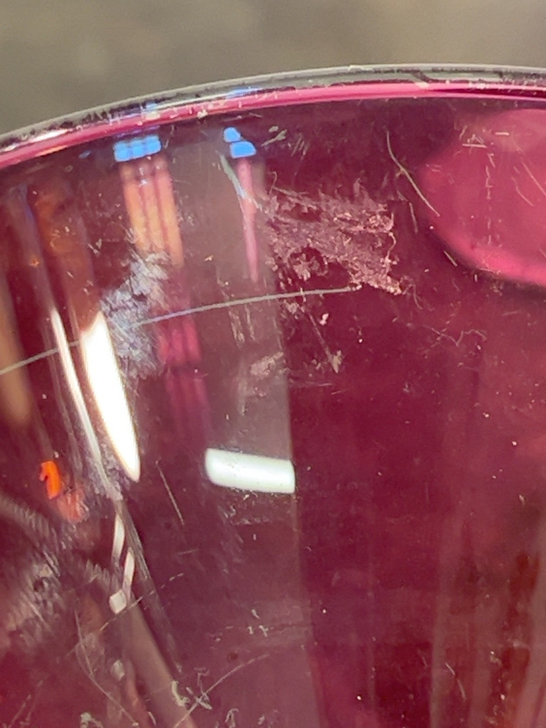 Close-up of surface scratches and wear on ruby red cocktail glass